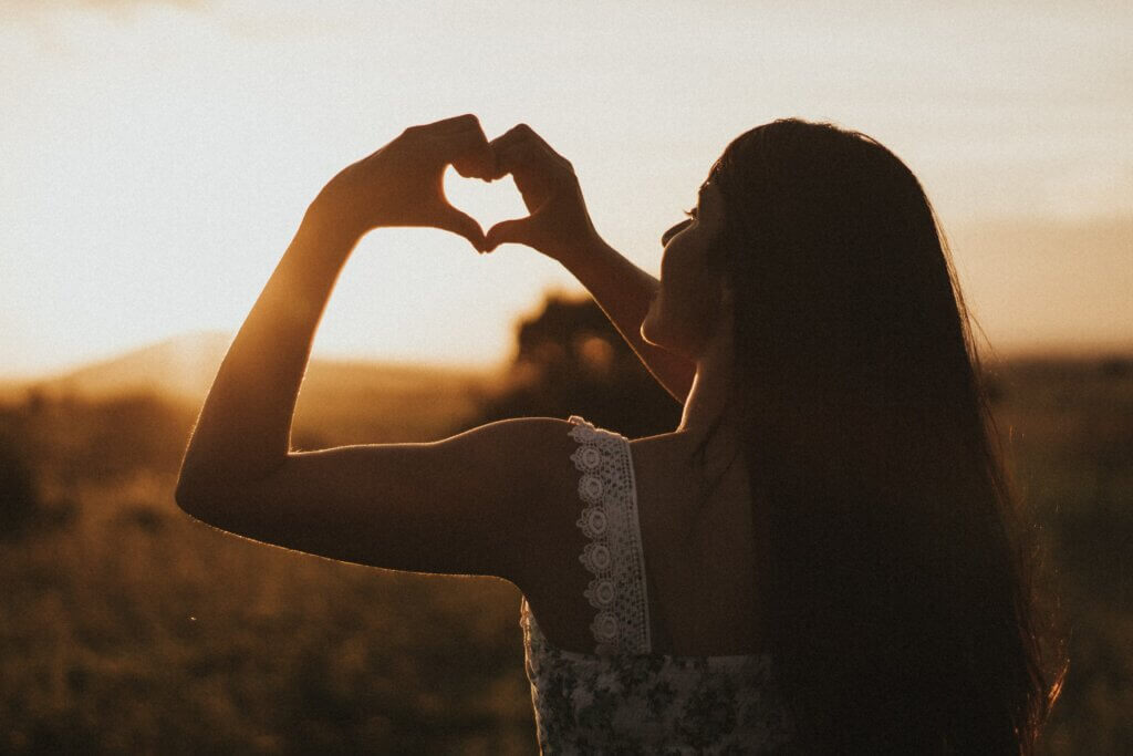 Une femme de dos faisant un coeur avec les mains.