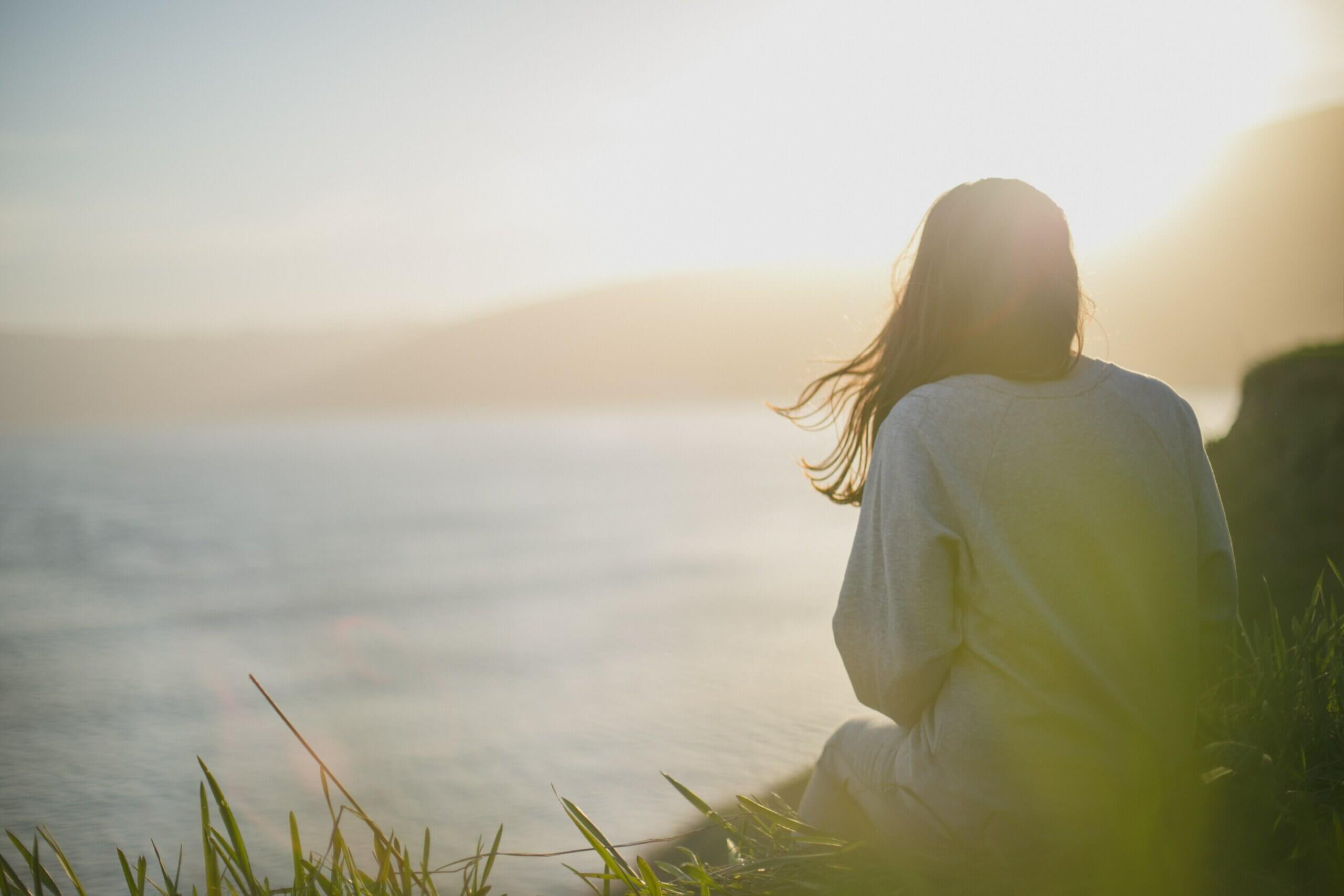 Une femme face à un lac en pleine nature.