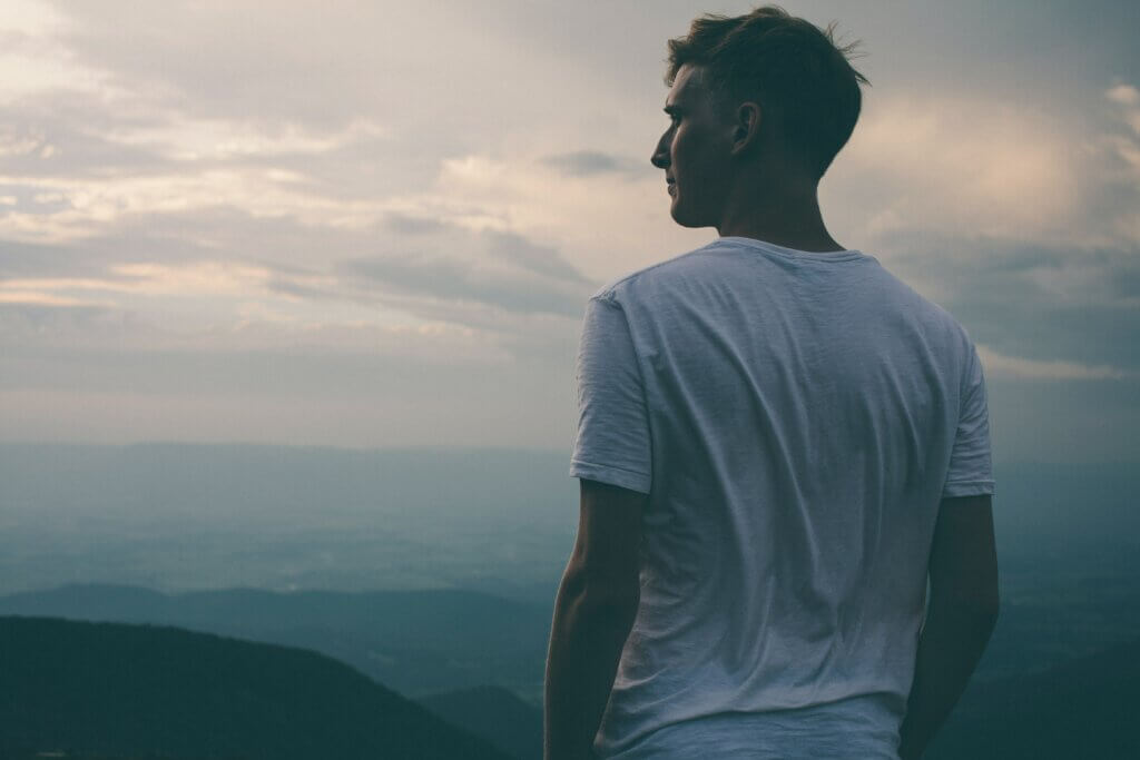 Un homme de dos au sommet d'une montagne et contemplant la vue.