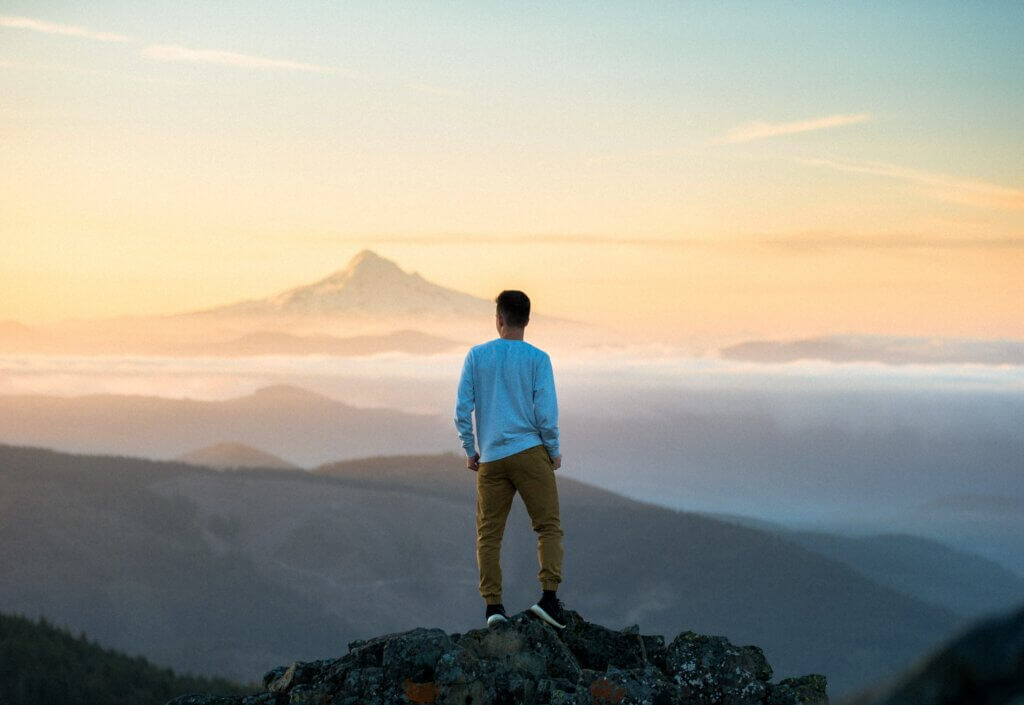 Un jeune homme de dos au sommet d'une montagne et contemplant la vue.